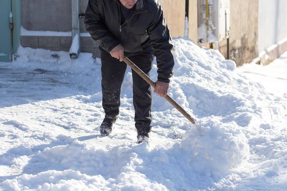 Mand skovler sne foran hus